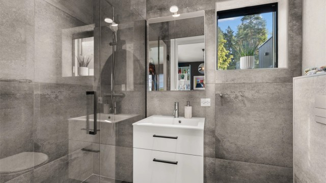 Master-badet holder en moderne og smakfull standard med store flislagte overflater, gulvvarme og downlights i tak. Badet er innredet med vegghengt servantinnredning, speil med belysning, vegghengt toalett og en romslig dusjsone.
