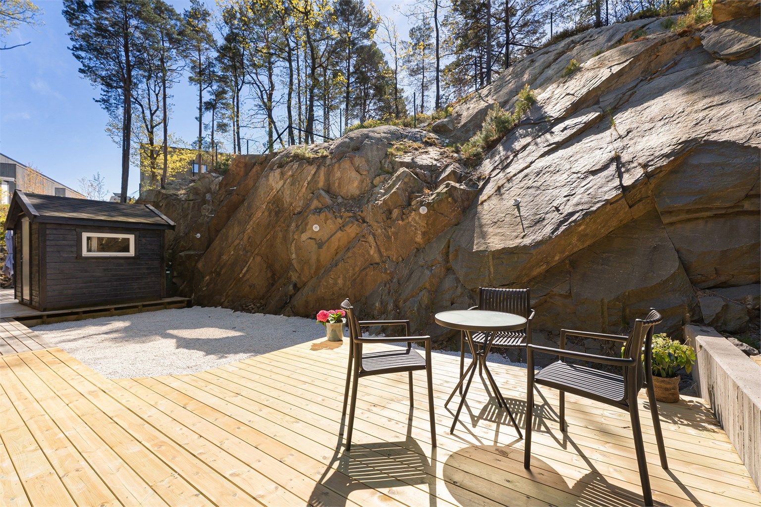 Uteområde på bakside som går i ett med naturen med terrasse og lyse stein som gir en kontrast til den moderne kledningen til huset