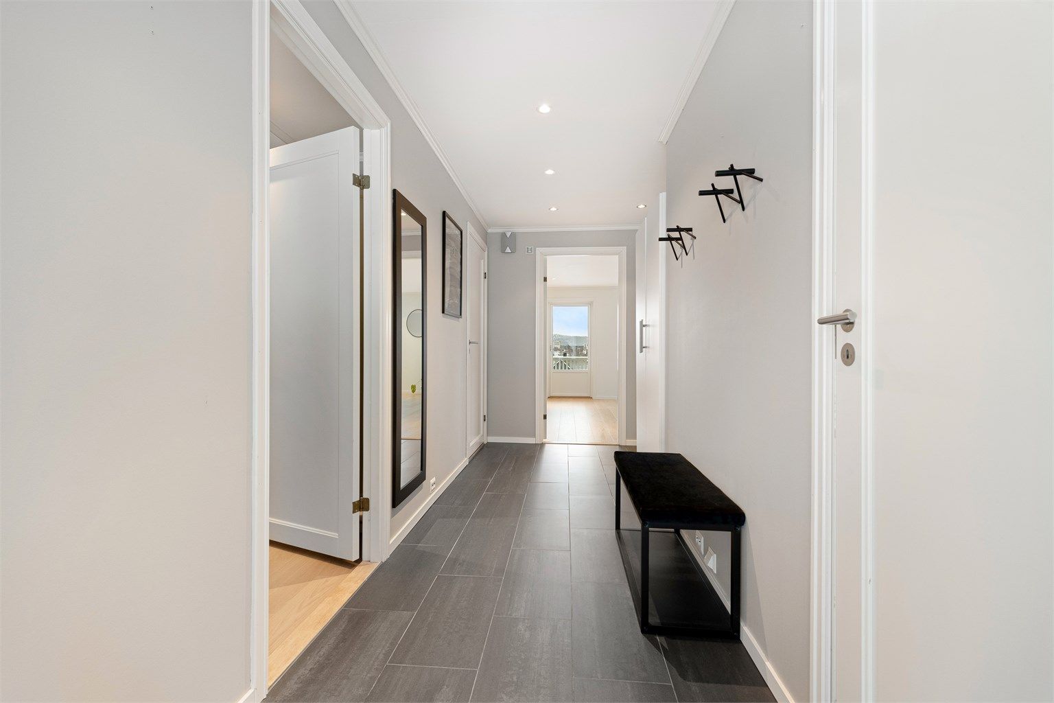 Lys og flislagt entre/gang med hvite profilerte innerdører og dør med glassfelt mot stue/kjøkken