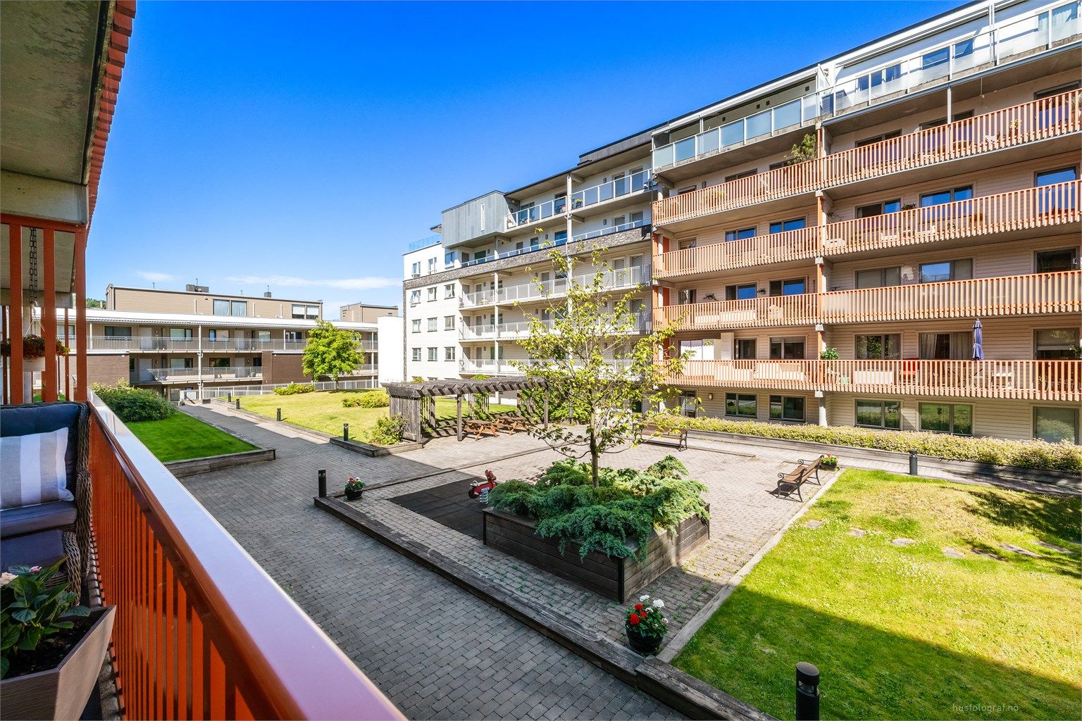 Balkongen har utsikt mot fine fellesarealer og ettermiddagssol (midtsommerstid).