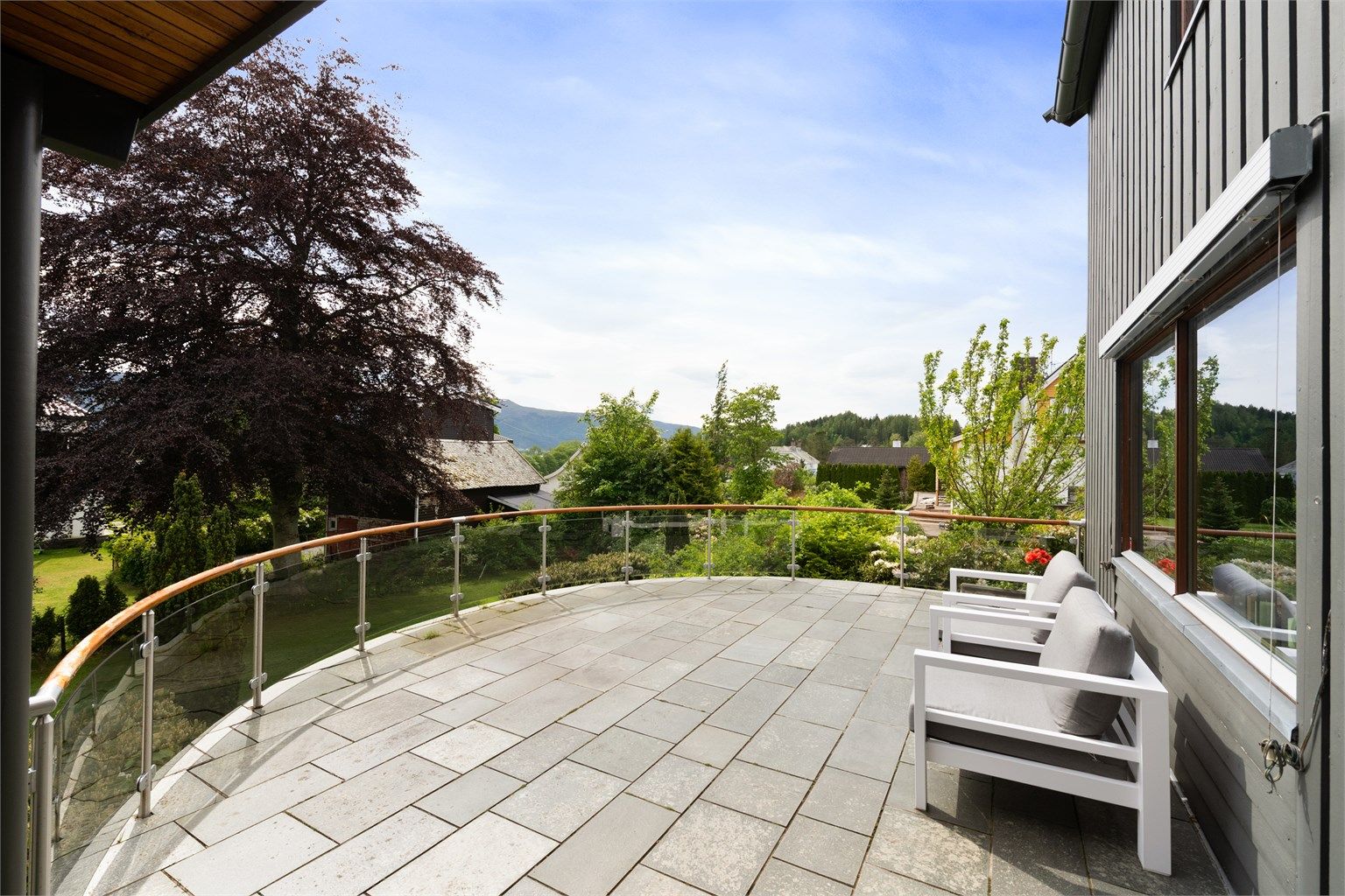 Skiferbelagt terrasse med rekkverk i glass og trehåndrekke med god plass til utemøbler.