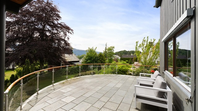Skiferbelagt terrasse med rekkverk i glass og trehåndrekke med god plass til utemøbler.