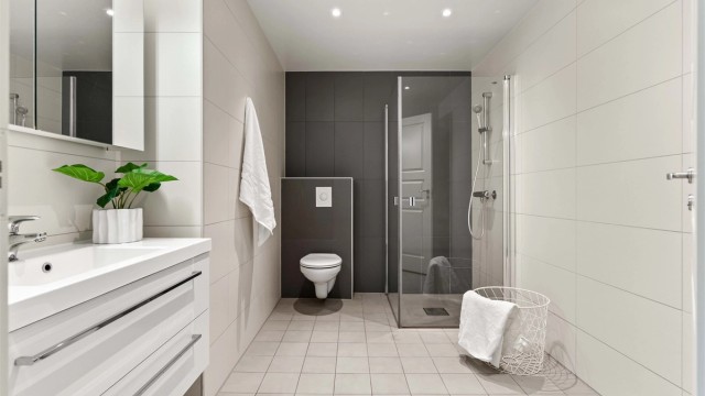 Stilrent, flislagt baderom med moderne innredning. Badet er utstyrt med vegghengt toalett, romslig servantmøbel med gode skuffer og lekkert dusjhjørne med innfellbare glassdører. Downlights i taket og nøytrale fargevalg skaper en behagelig atmosfære.
