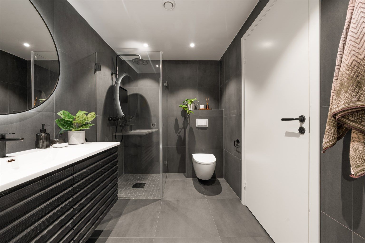 Delikat, flislagt bad med moderne innredning, vegghengt toalett og en romslig dusjsone.