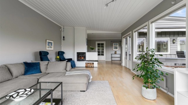 Stor og lys stue med flere soner, peis i hjertet av rommet og utgang til terrasse