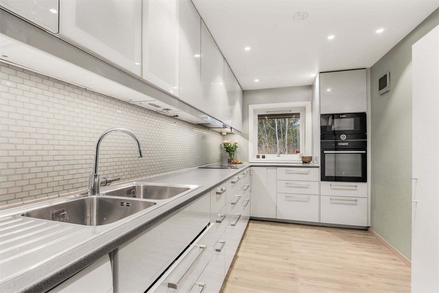 Kjøkkeninnredning fra 2017 med glatte fronter, laminatbenkeplate og fliser over benken.