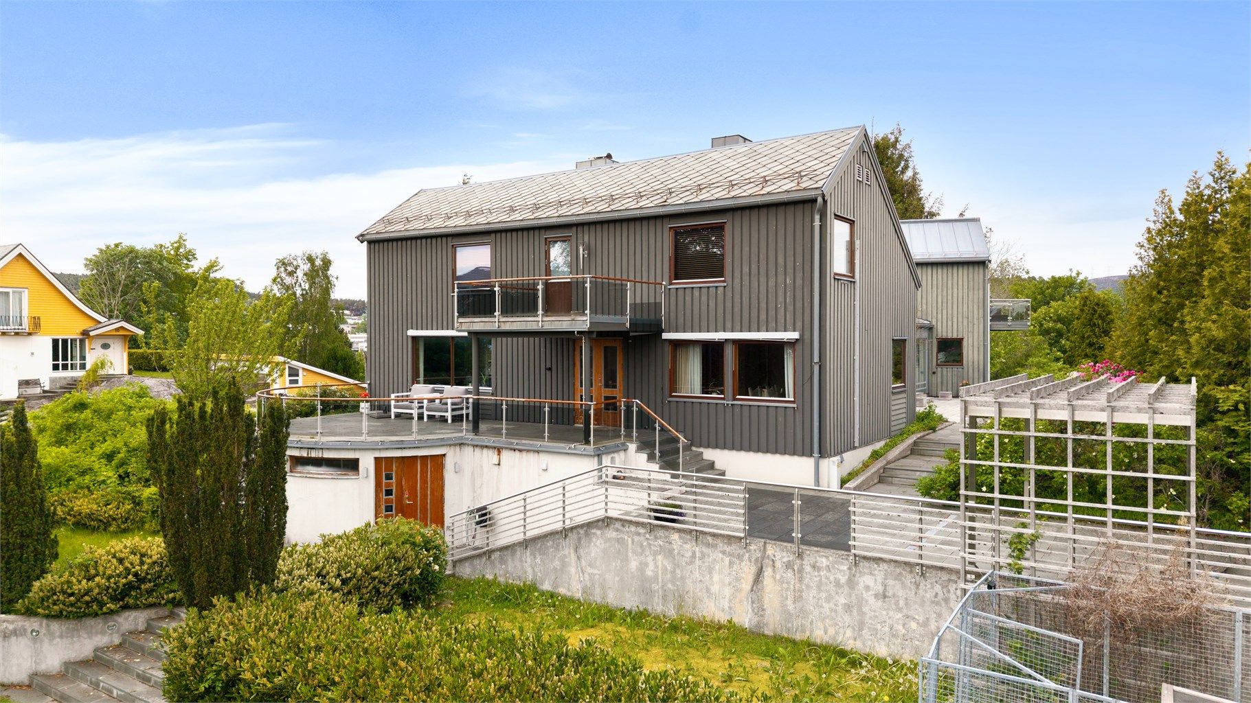 Søndre fasade med store terrasseflater og trappeløp i skifer ned mot hagen.