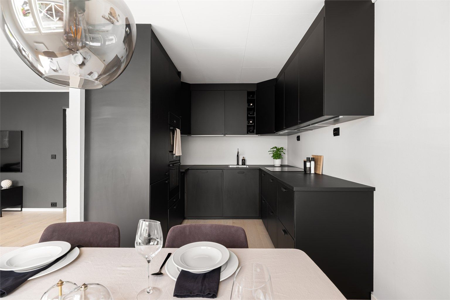 Romslig åpen stue- og kjøkkenløsning med kjøkkeninnredningen praktisk plassert avsides fra stuen.