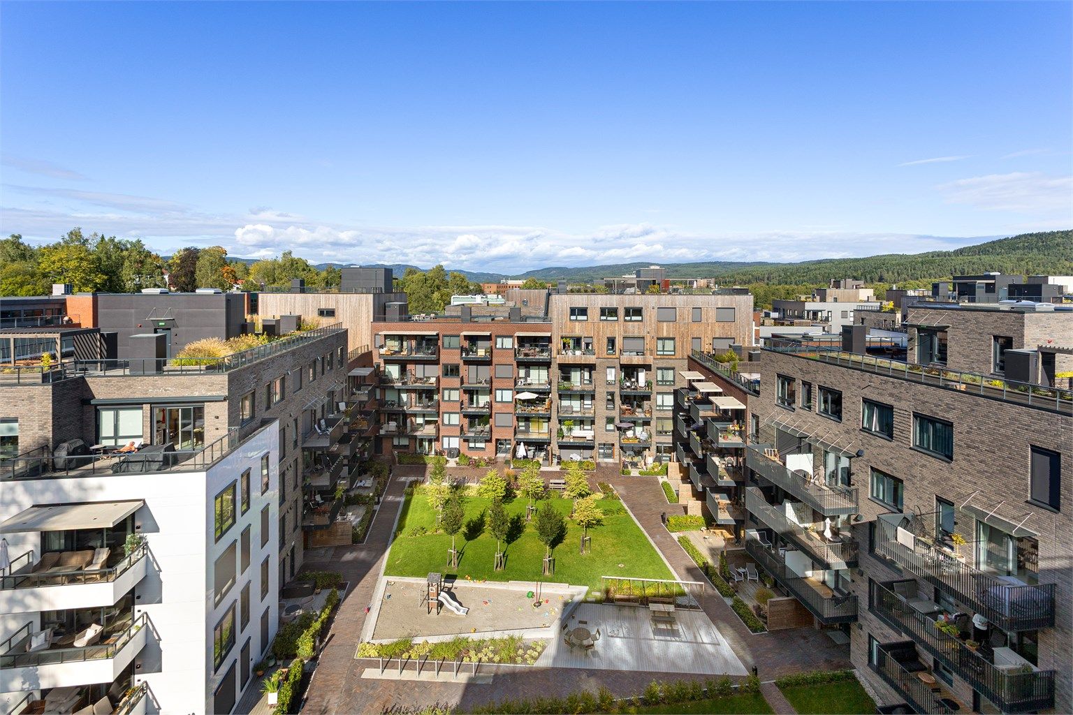 Gårdsrommet har lekeplass, sittebenker og frodige plenarealer.