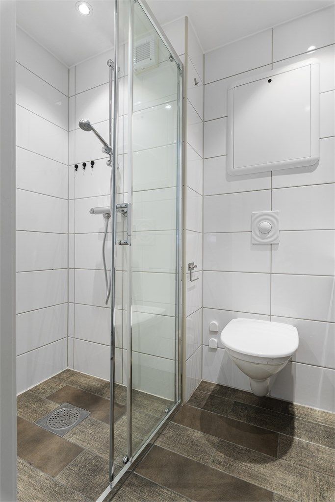 Badet er kompakt, men er utstyrt med alt det nødvendige. Praktisk dusjnisje med skyvedør og dusjgarnityr, samt vegghengt toalett