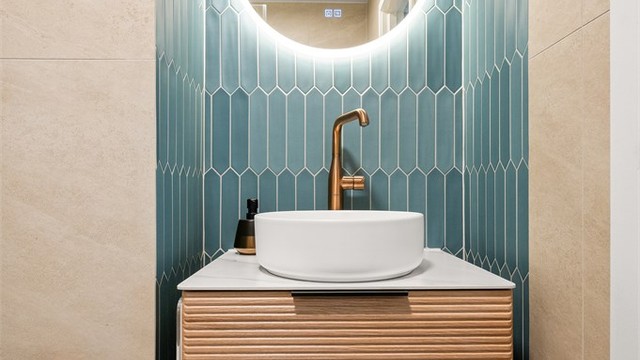 Badet har flislagt gulv med gulvvarme, flislagte vegger og stilren innredning med vegghengt servantmøbel, speil med lys og vegghengt toalett.