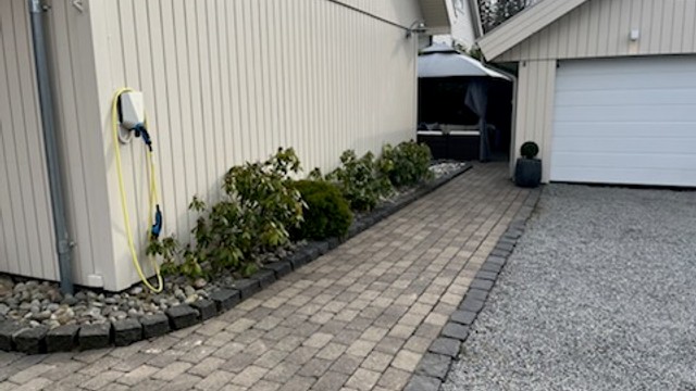 Pent opparbeidet uteareal, med Herregaardsten, gruset innkjørsel, bedd og beplantinger.