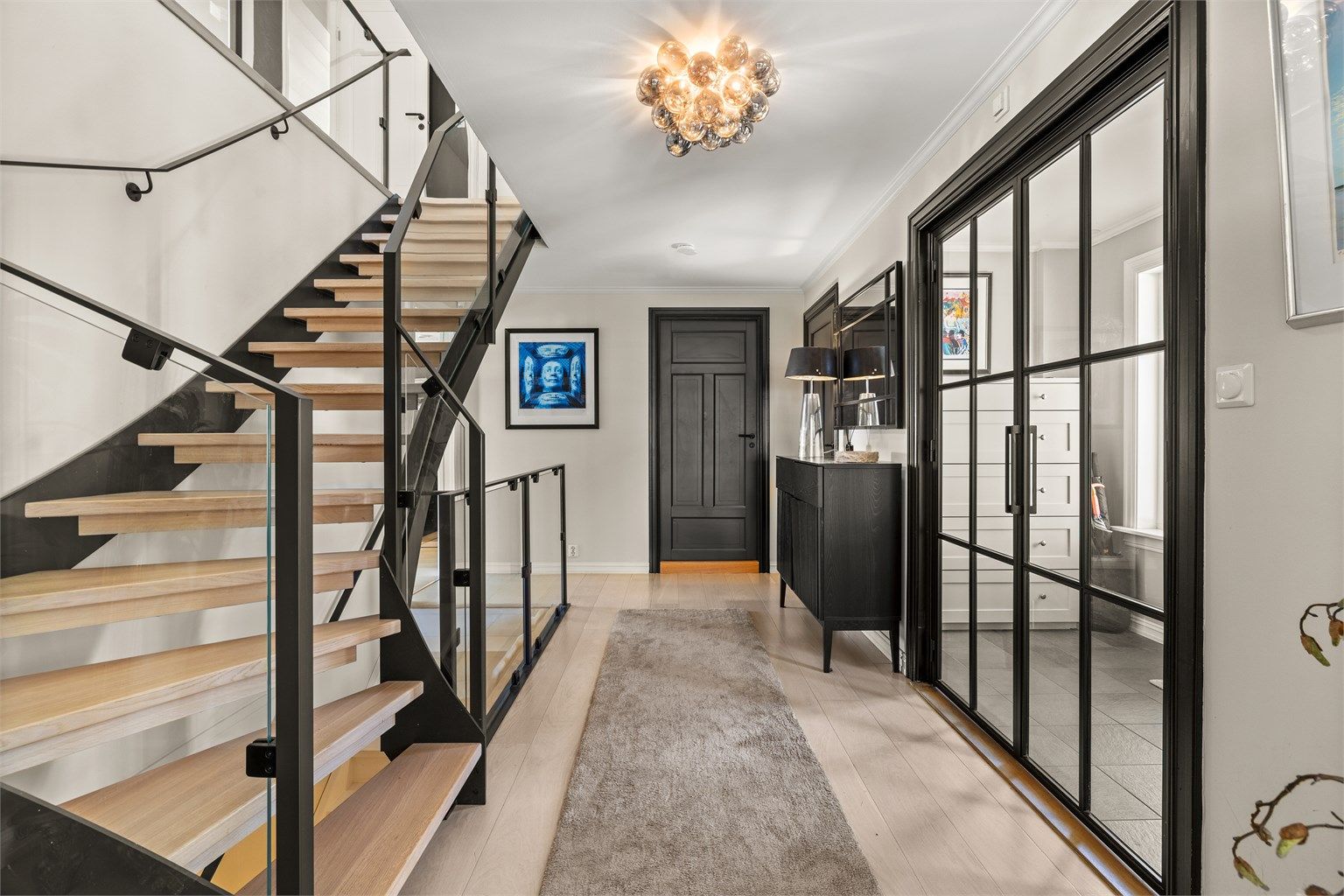 Hall med 1-stavs parkett med vannbåren gulvvarme. Fra hallen er det adkomst til stuen, kjøkkenet, toalettet og vaskerommet. Doble smijernsdører inn til stuen. Fra hallen går også trappene til de øvrige etasjene. Trappen til 2. etasje var ny i 2021