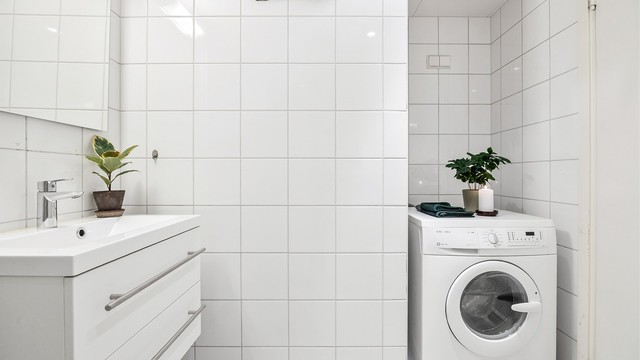 Videre er det dusjhjørne med dører, vegghengt toalett og opplegg for vaskemaskin.