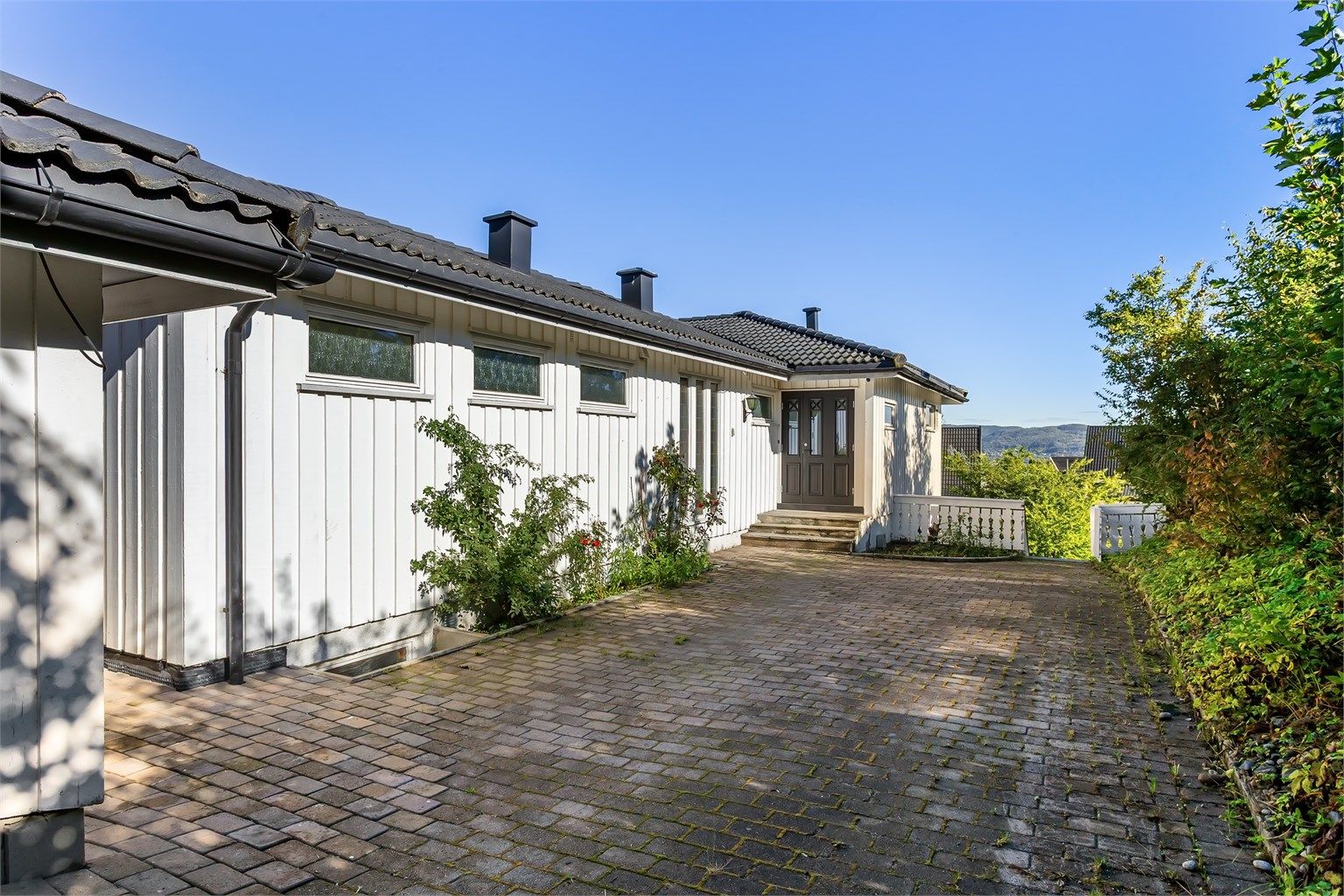 Innkjøring og gårdsplass er belagt med belegningsstein, med parkering foran garasjen.