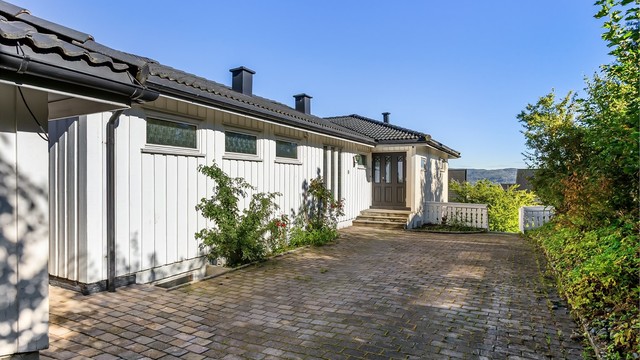 Innkjøring og gårdsplass er belagt med belegningsstein, med parkering foran garasjen.
