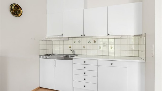 Kjøkkeninnredning med glatte fronter, laminert benkeplate, platetopp og kjøleskap.