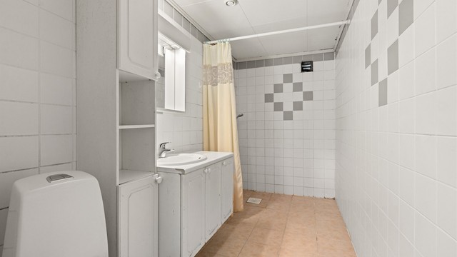 Badet er innredet med toalett, servant og dusjhjørne med forheng.
