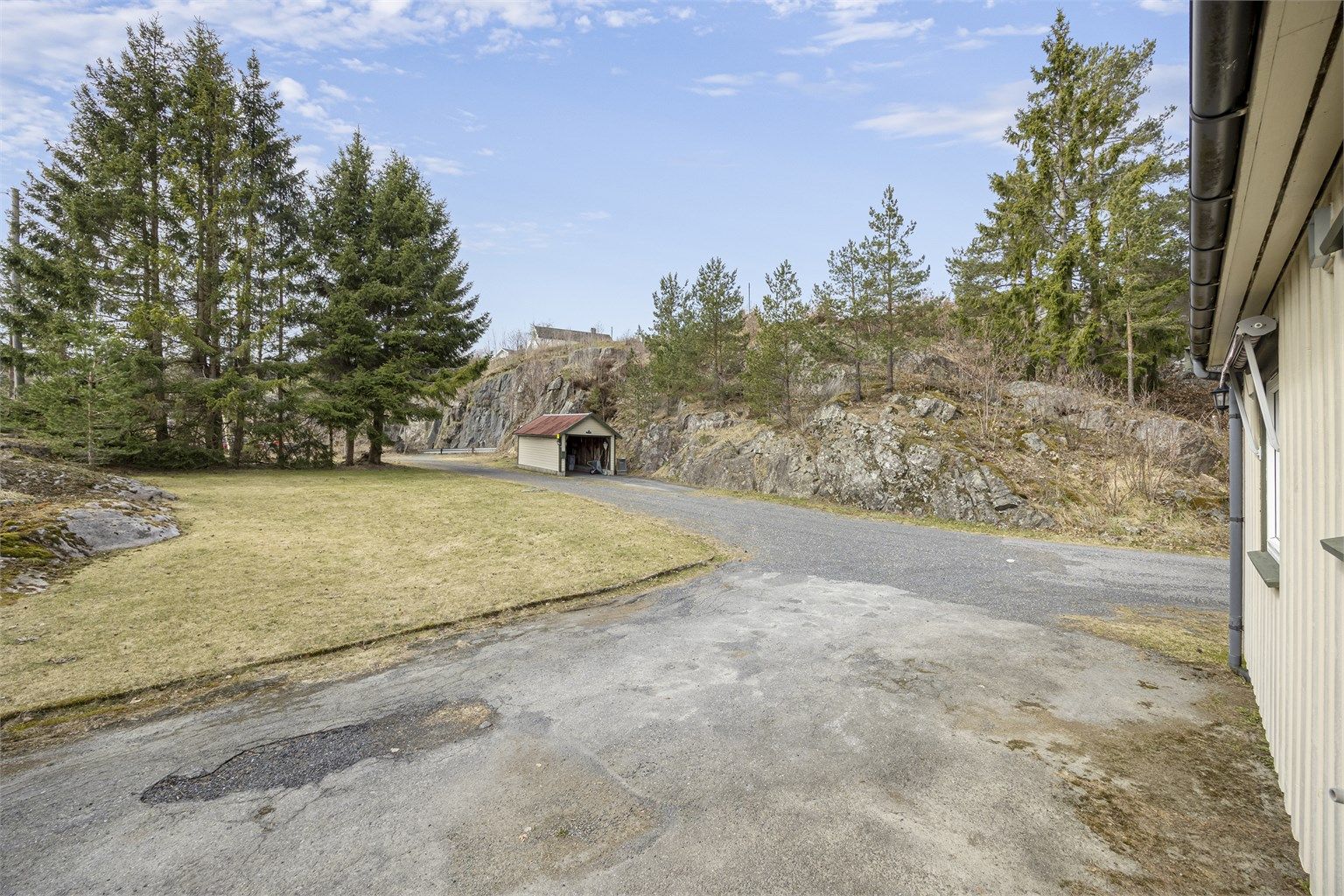 Garasje og store plenarealer, samt romslig, gruset tun på veien forbi garasjen.