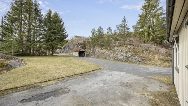 Garasje og store plenarealer, samt romslig, gruset tun på veien forbi garasjen.