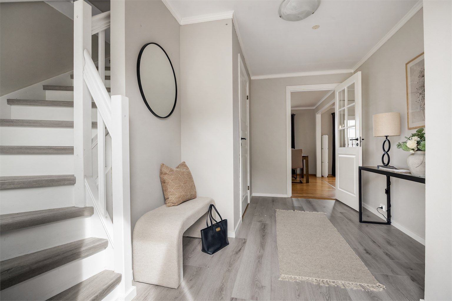 Lys og innbydende hall med nytt laminatgulv fra 2024. Trappen har laminat i trinnene og malt rekkverk.