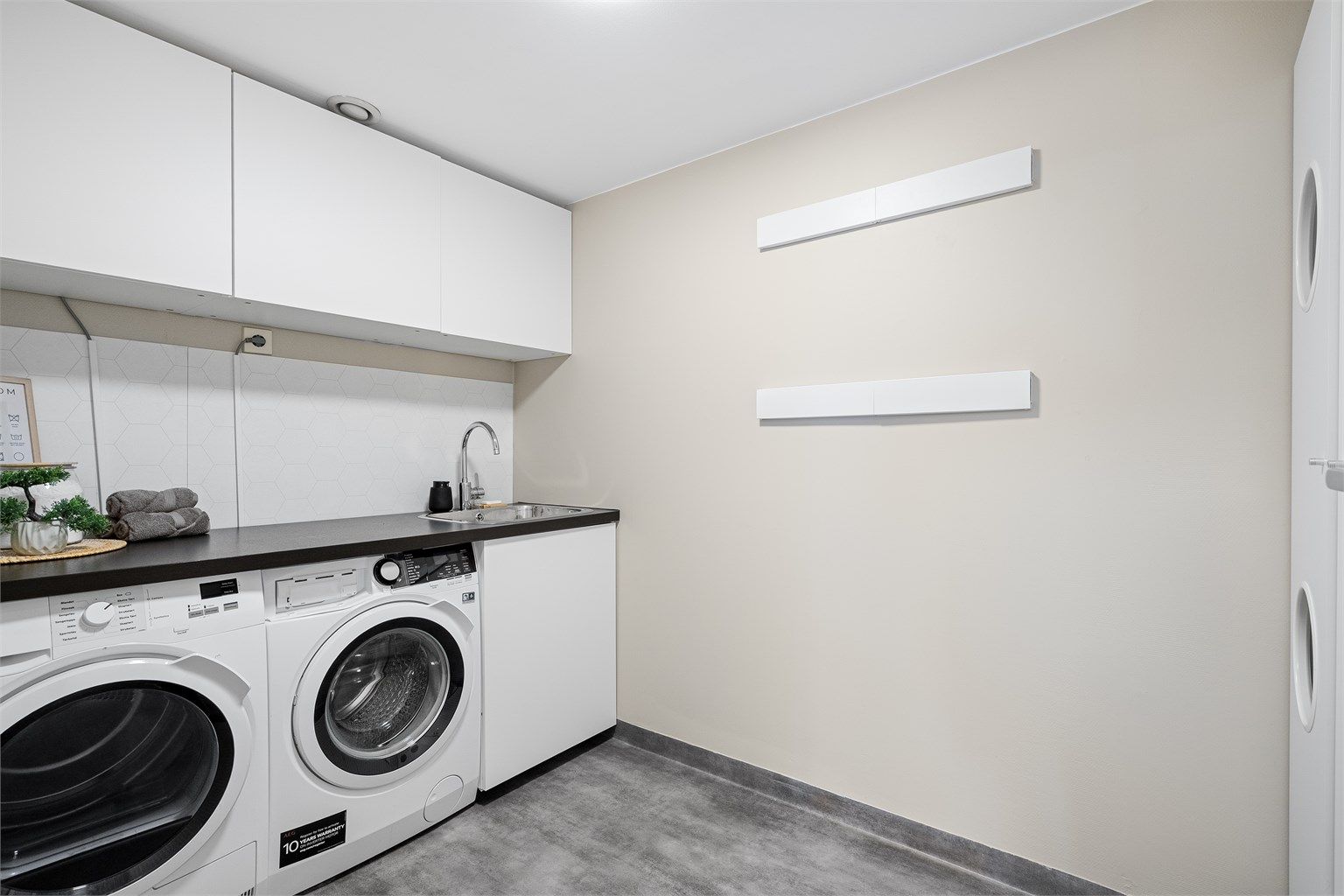 
Vaskerom er av god størrelse og praktisk innredet med vaskemaskin og tørketrommel ved siden av hverandre, benkeplate og skap til oppbevaring. Det er belegg på gulv og malte vegger. Det er også utslagsvask på rommet. 