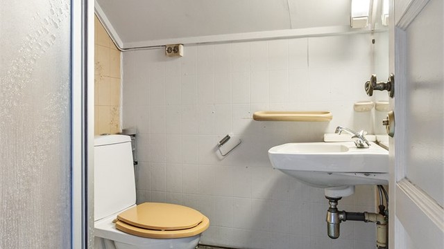 Baderom med vegghengt servant, speil med overlys, dusjkabinett og gulvstående toalett. Gulvbelegg på gulv og tapet på vegger.