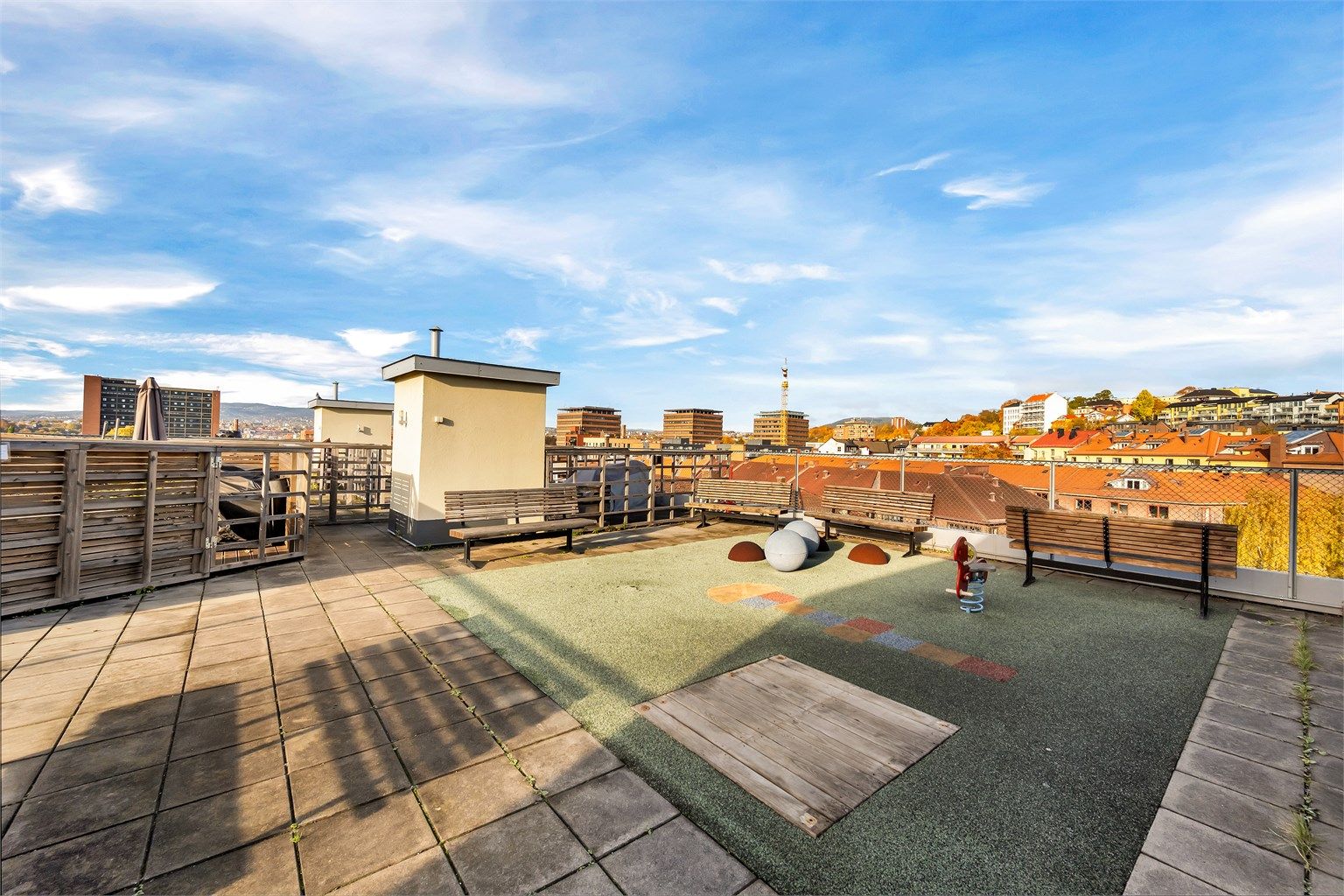 Stor felles takterrasse med lekeareal, benker og vid utsikt over byen.