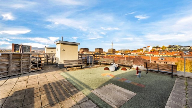Stor felles takterrasse med lekeareal, benker og vid utsikt over byen.
