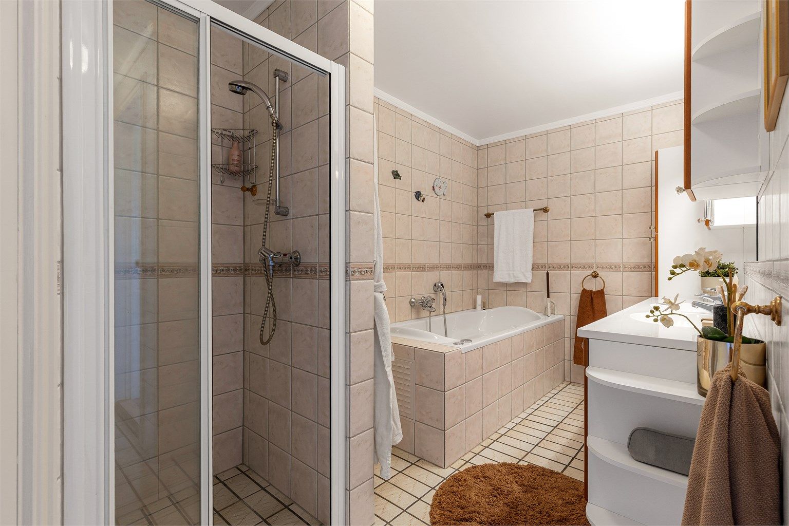 Vegghengt skap ved speil. Dusjhjørne med skyvedør av glass og metall. Vegghengt dusjarmatur. Flislagt boblebadekar. Vegghengt dusjarmatur.