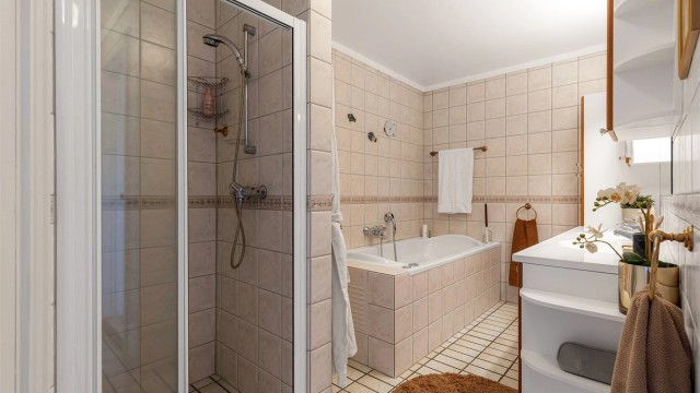 Vegghengt skap ved speil. Dusjhjørne med skyvedør av glass og metall. Vegghengt dusjarmatur. Flislagt boblebadekar. Vegghengt dusjarmatur.