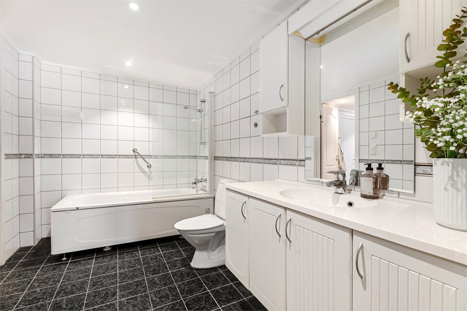 Badet er flislagt og har en større servant med oppbevaring samt tilhørende overskap. 