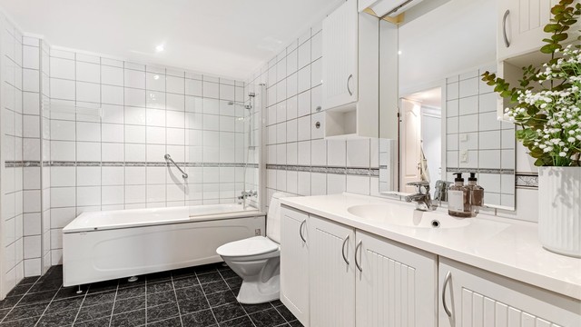 Badet er flislagt og har en større servant med oppbevaring samt tilhørende overskap.