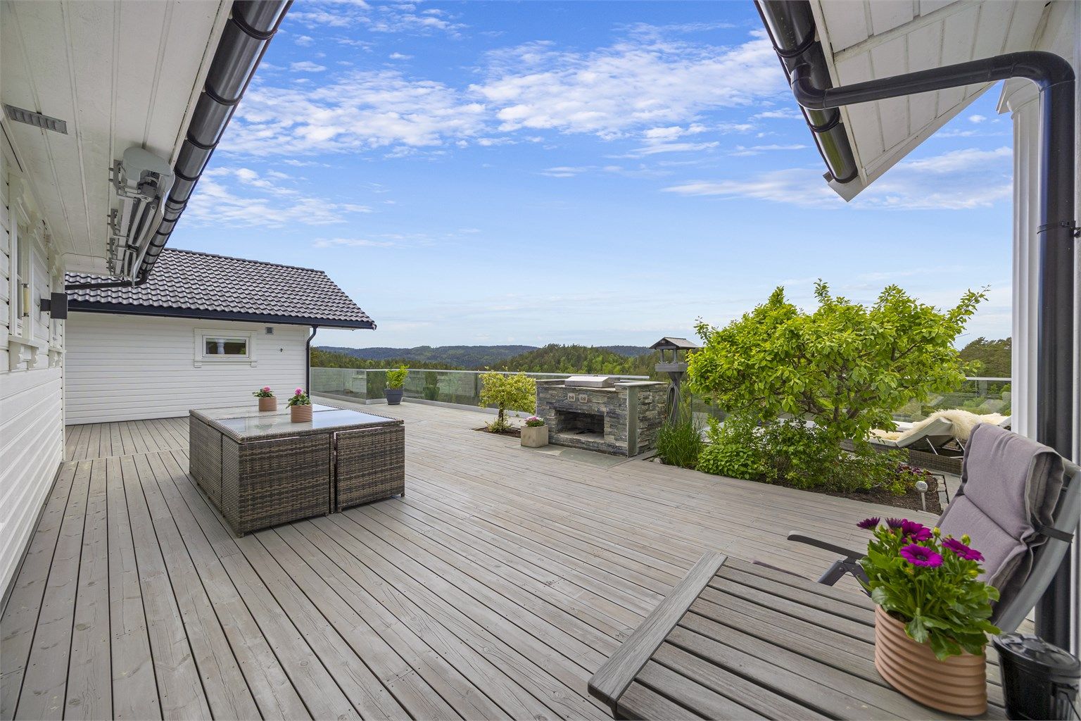Terrassen strekker seg langs hele baksiden av huset og er bygget i trekonstruksjoner med rekkverk av metall og glass. Natursteinsgrill medfølger.
