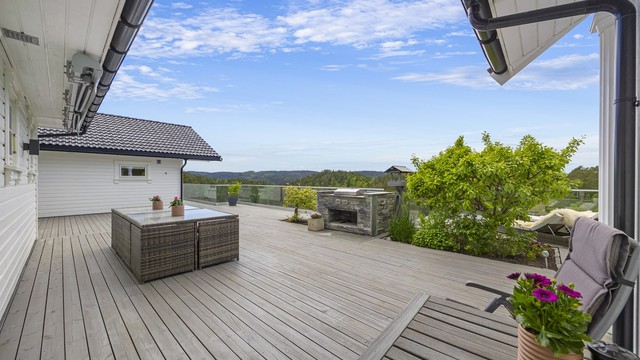 Terrassen strekker seg langs hele baksiden av huset og er bygget i trekonstruksjoner med rekkverk av metall og glass. Natursteinsgrill medfølger.