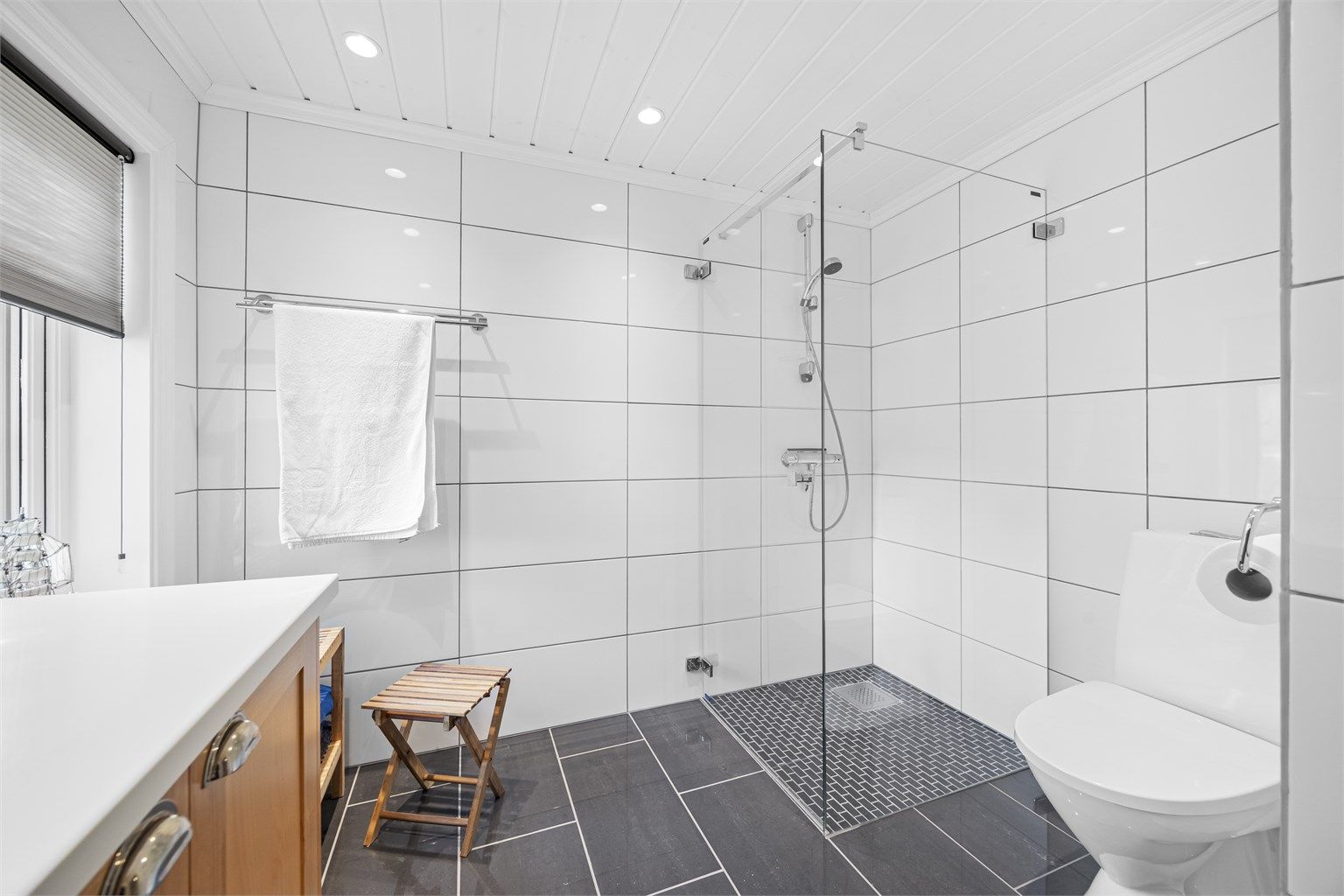 Badet er utstyrt med dusjnisje med glassdør, vegghengt servantinnredning og gulvstående toalett.