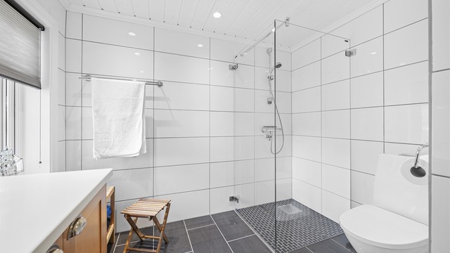 Badet er utstyrt med dusjnisje med glassdør, vegghengt servantinnredning og gulvstående toalett.