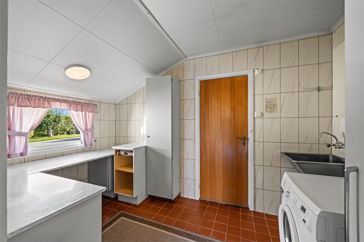 Separat vaskerom med fliser på vegger og gulv, skyllekar, benkeplate og opplegg for vaskemaskin.