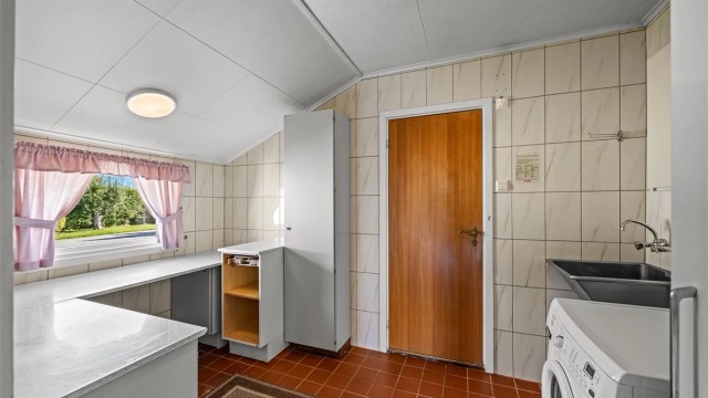Separat vaskerom med fliser på vegger og gulv, skyllekar, benkeplate og opplegg for vaskemaskin.