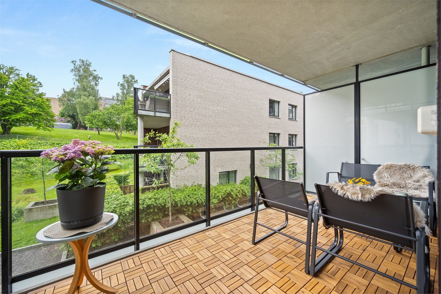 Balkongen er utført i betong med tremmer av tre på gulvet, og har et rekkverk i glass og metall.