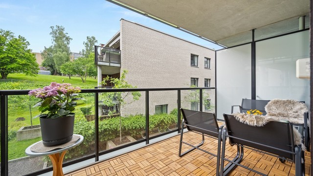 Balkongen er utført i betong med tremmer av tre på gulvet, og har et rekkverk i glass og metall.