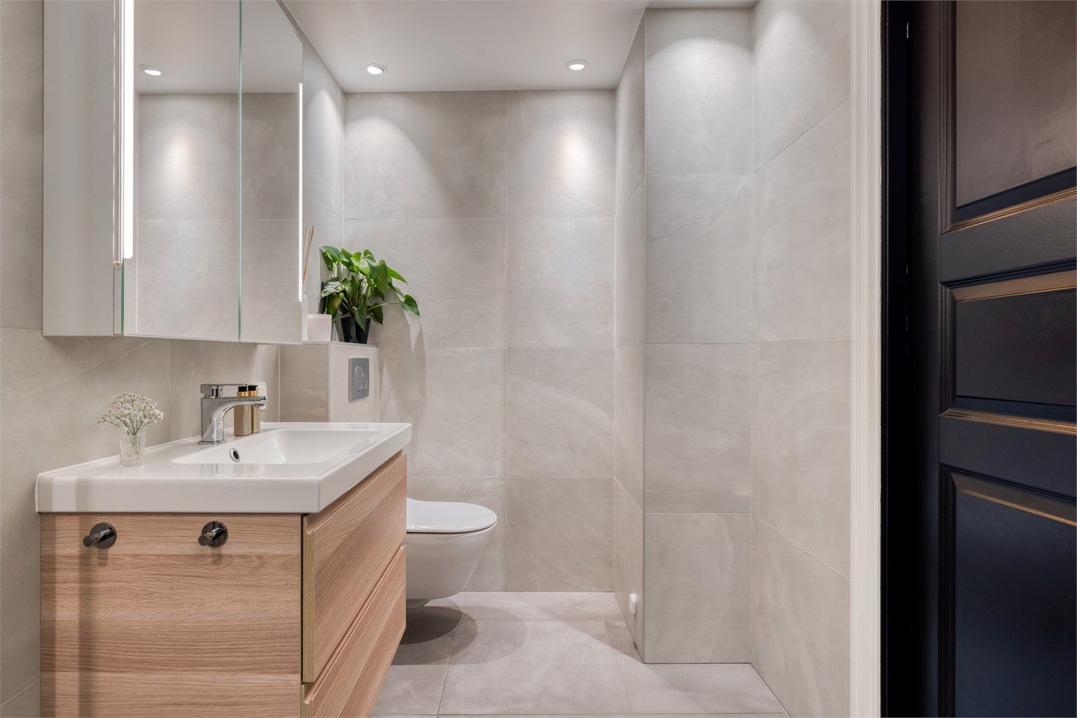 Badet er innredet med skap og ovenpåliggende servant, speilskap med belysning, vegghengt toalett.