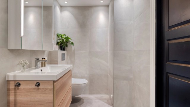 Badet er innredet med skap og ovenpåliggende servant, speilskap med belysning, vegghengt toalett.