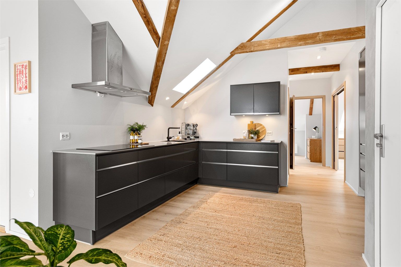 Den åpne løsningen mellom kjøkken og stue skaper en sosial og inkluderende atmosfære, med gjennomgående laminatgulv som binder sonene sammen.