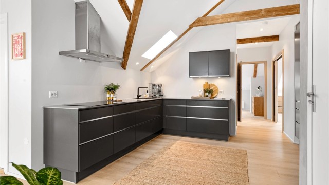 Den åpne løsningen mellom kjøkken og stue skaper en sosial og inkluderende atmosfære, med gjennomgående laminatgulv som binder sonene sammen.