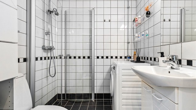 Badet er flislagt på gulv og vegger med elektrisk gulvvarme. Badet er innredet med dusjhjørne med svingbare glassdører, toalett og servant med innredning.