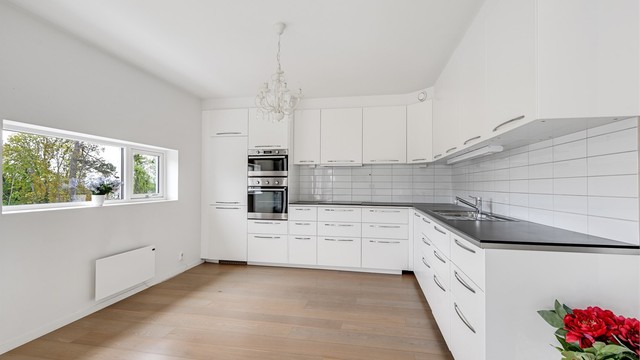 Kjøkkenet har innredning med glatte fronter. Benkeplaten er av laminat. Det er kjøl/fryseskap, oppvaskmaskin, induksjonstopp, mikrobølgeovn og stekeovn integrert i innredningen.