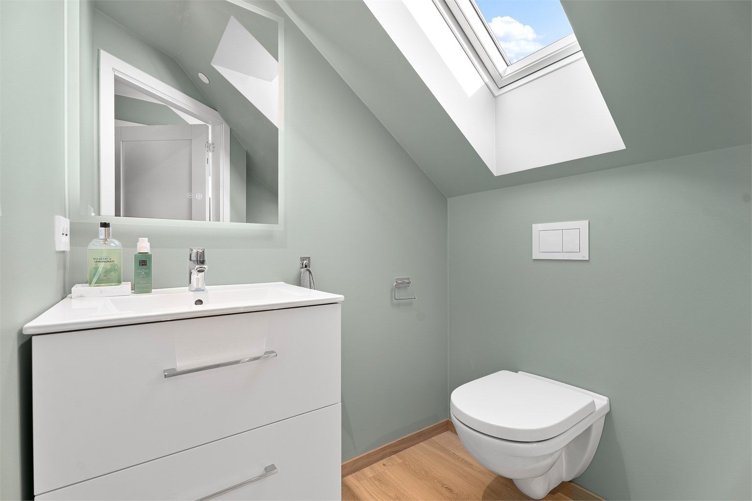 Toalettrom med vegghengt toalett, servant med oppbevaring samt speil. 