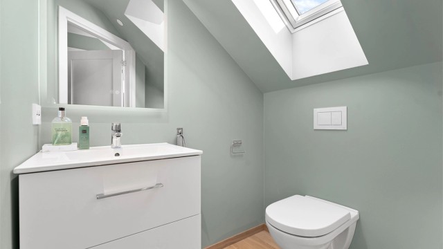 Toalettrom med vegghengt toalett, servant med oppbevaring samt speil.