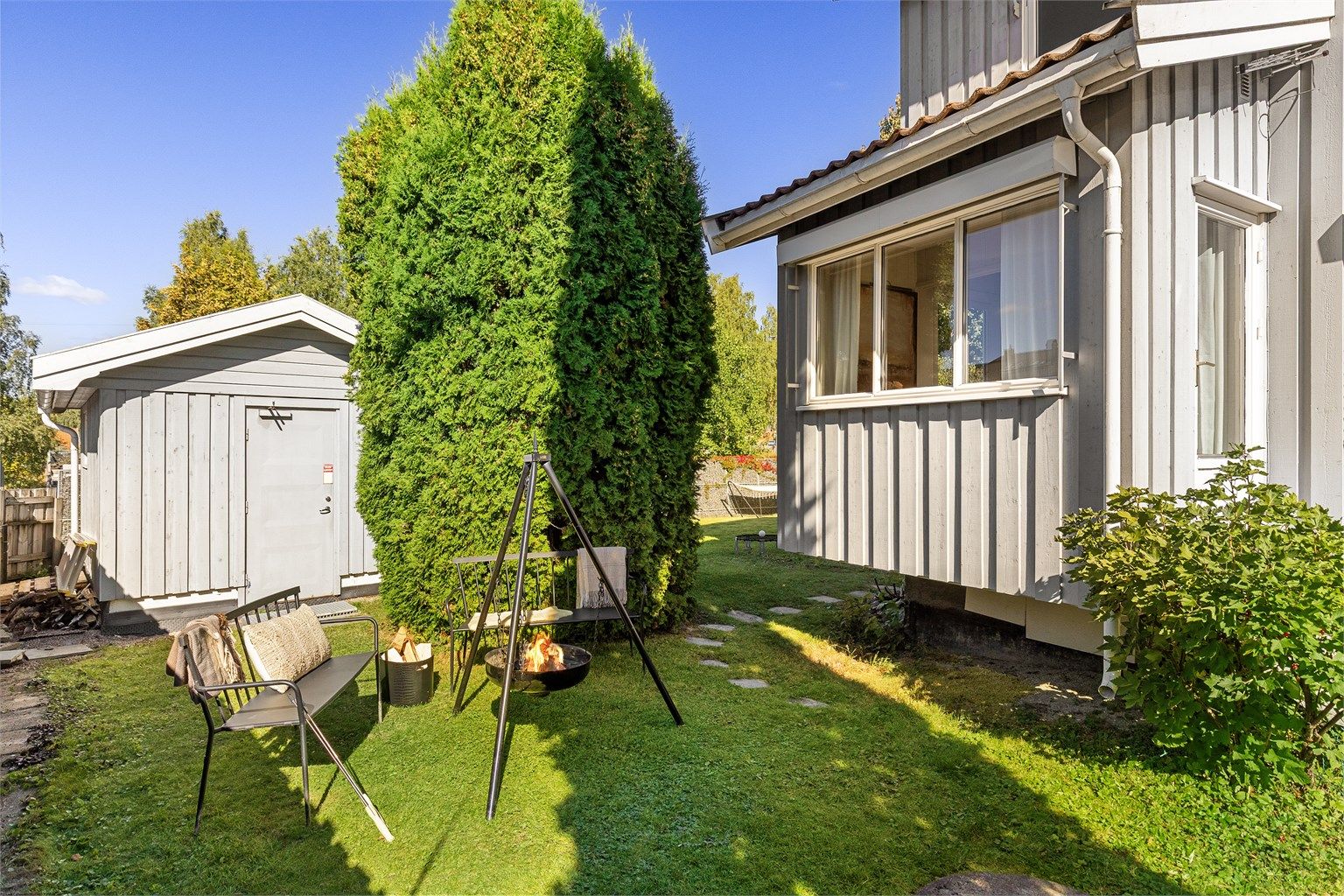Skjermet hageområde med frodig hekk og gangsti bort til uteboden.